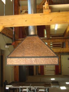 A copper ventilation hood in a workshop, possibly related to blacksmithing classes.