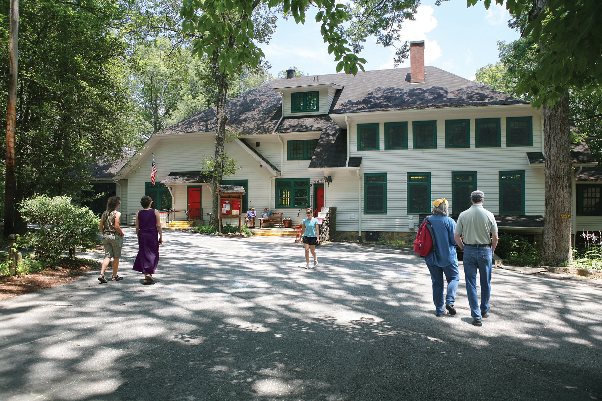 A group of people stands outside a large building with red accents and green-framed windows.