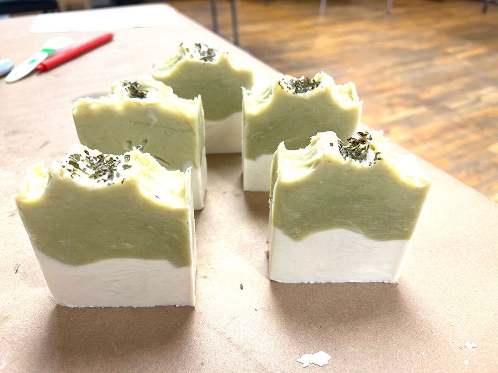 Five bars of green and white soap with an herb accouterment on top