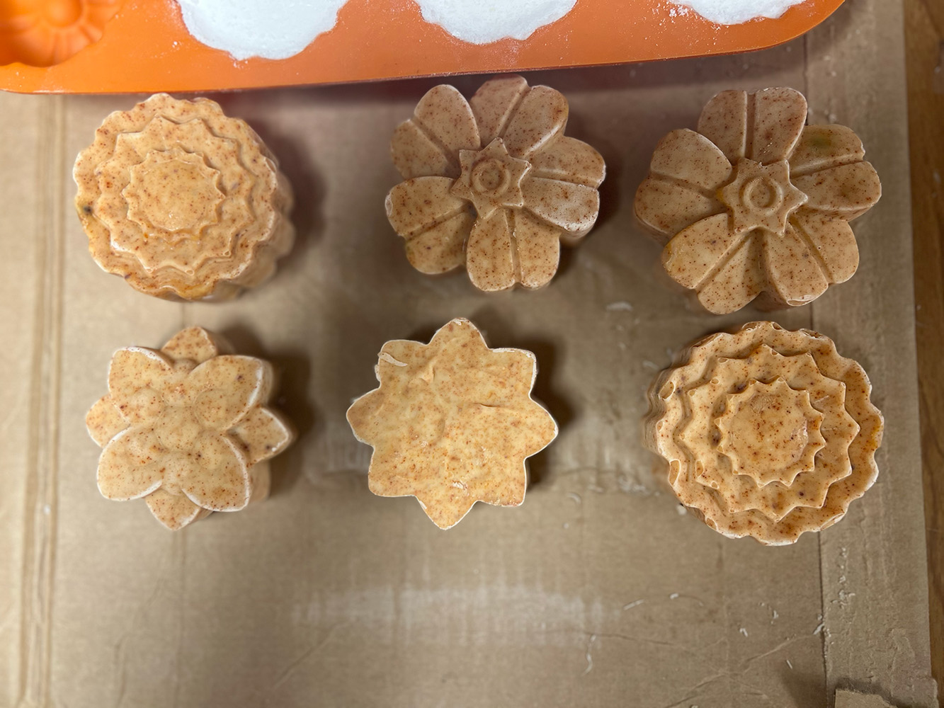 Six bars of soaps, arranged in two rows of three. Each bar was made from a mold and resembles a different flower design.