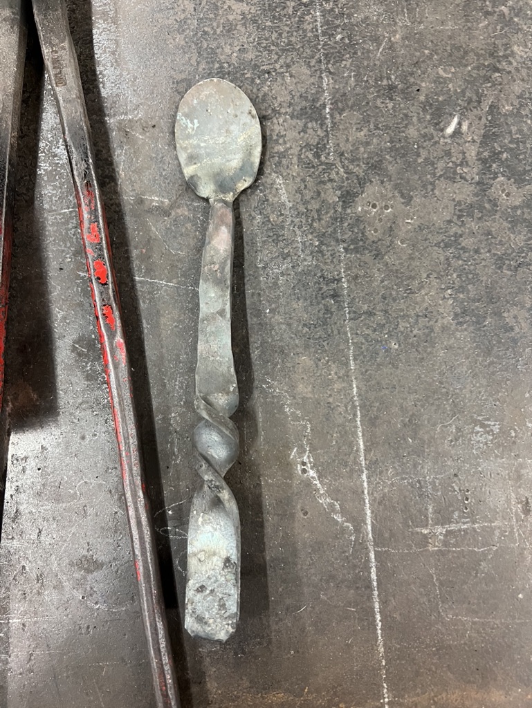A metal spoon on a table with one twist in the handle.
