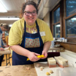 A young woman smiles for the camera while getting freshly-made soap out of one of the flower molds.