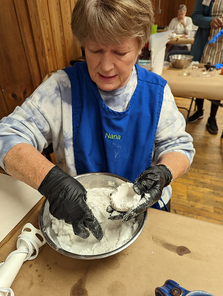 A woman mixes together raw material in a metal mixing bowl.