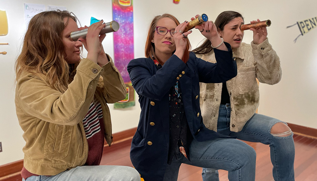 Three people looking into kaleidoscopes in the art gallery. Dezzy Moon, the subject of this article, is in the middle.