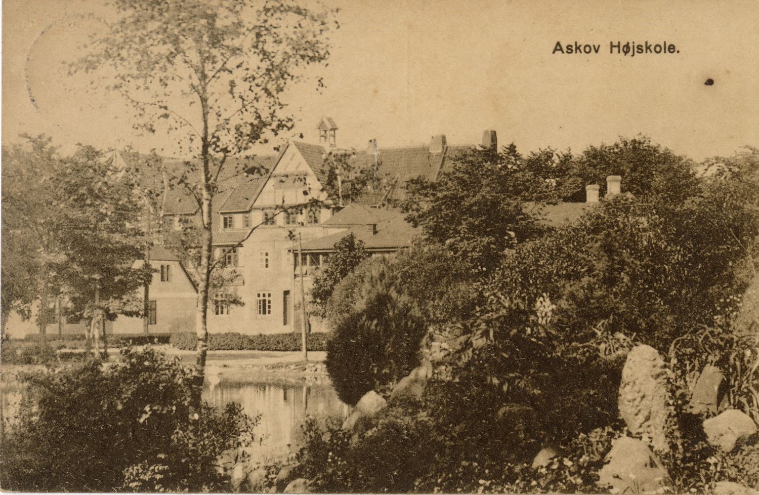 black-and-white postcard photograph of three-story building with trees and rocks in front, labeled "Askov Hojskole"
