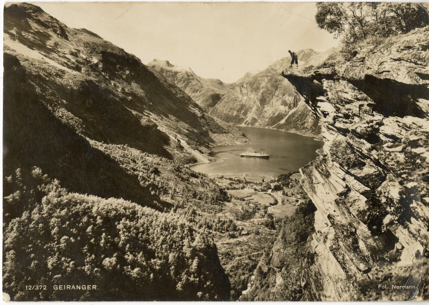 black-and-white postcard photograph of a boat in a lake in the middle of rocky mountains