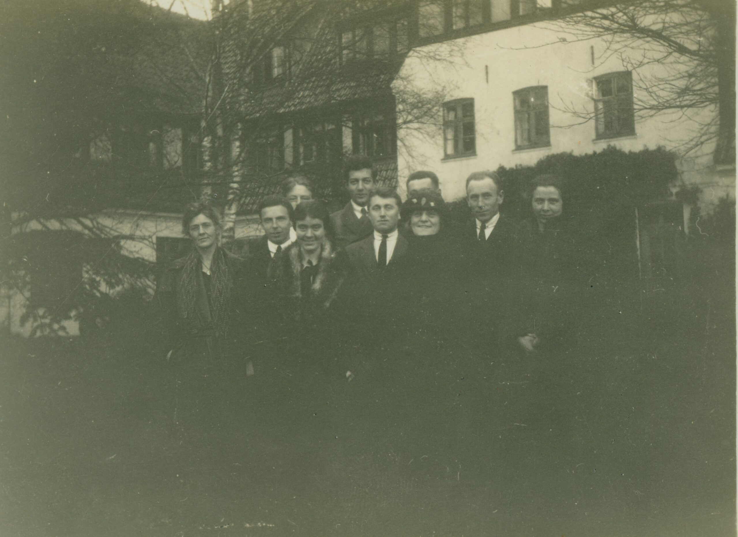 black-and-white photograph of a group of men and women standing in front of a three-story building
