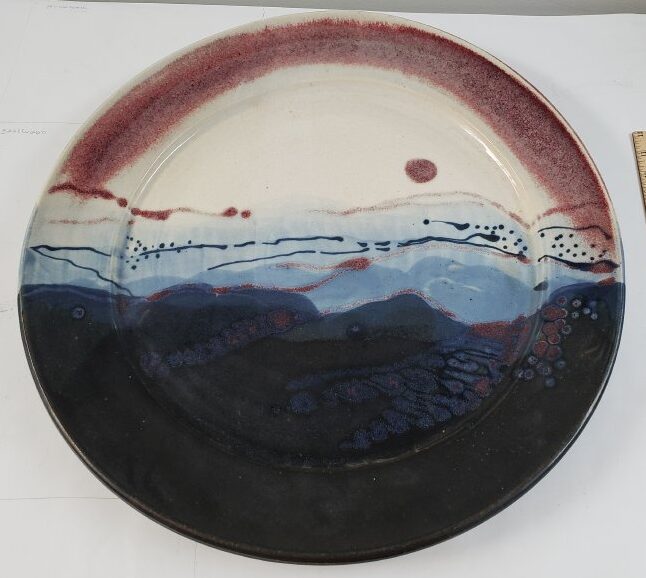 large porcelain plate, abstract mountain landscape in dark blue with lighter shades of blue and white representing sky and red spot for sun