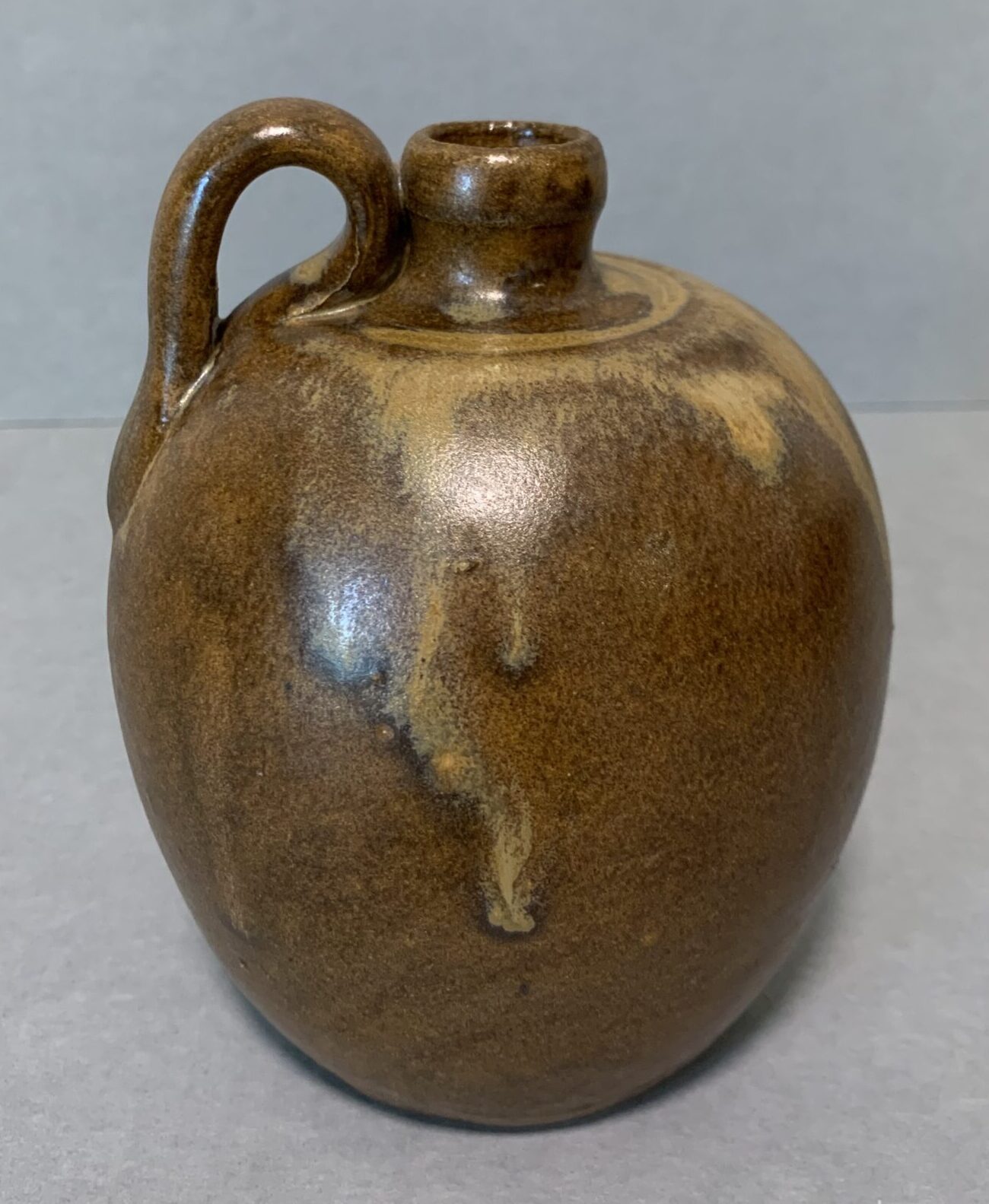 brown glazed ceramic jug with one handle and very small spout on top