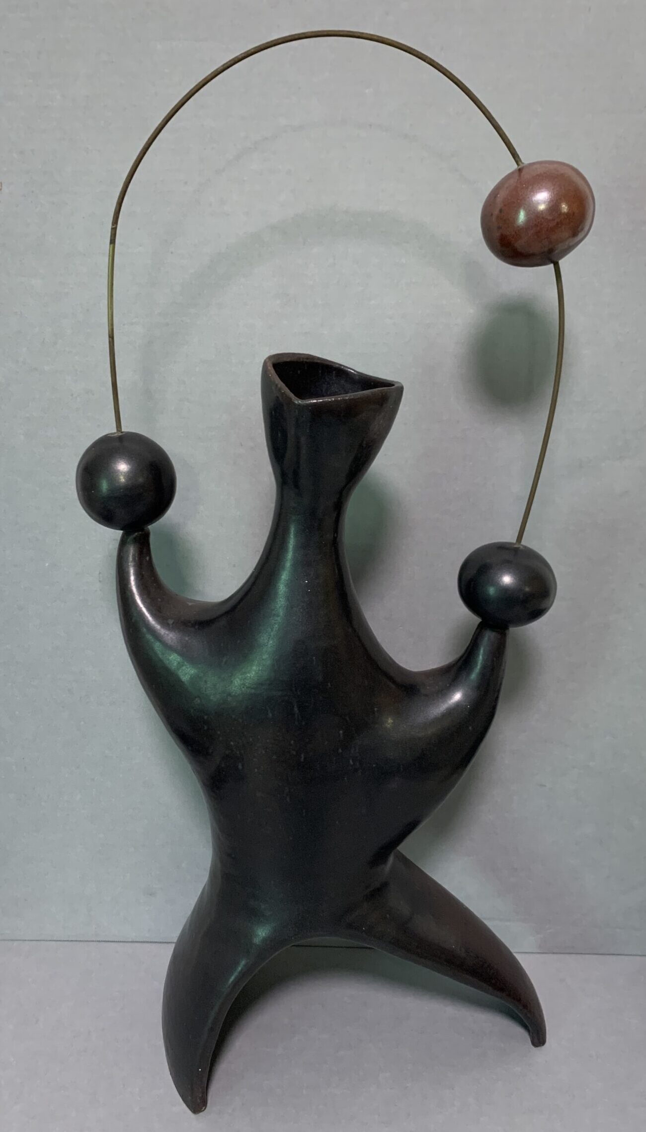 black ceramic vase sculpted into abstract human shape with wire loop holding three spheres
