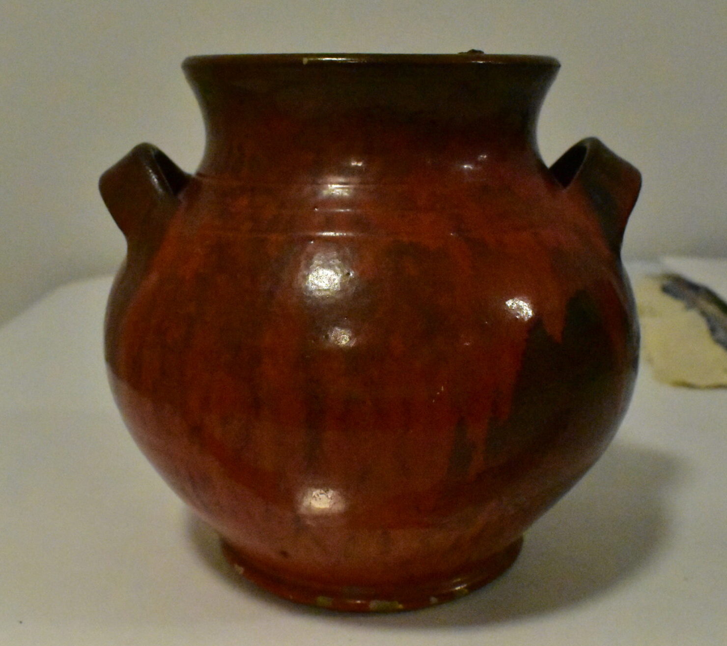 burnt-orange-colored glazed ceramic vessel, round shape with two handles