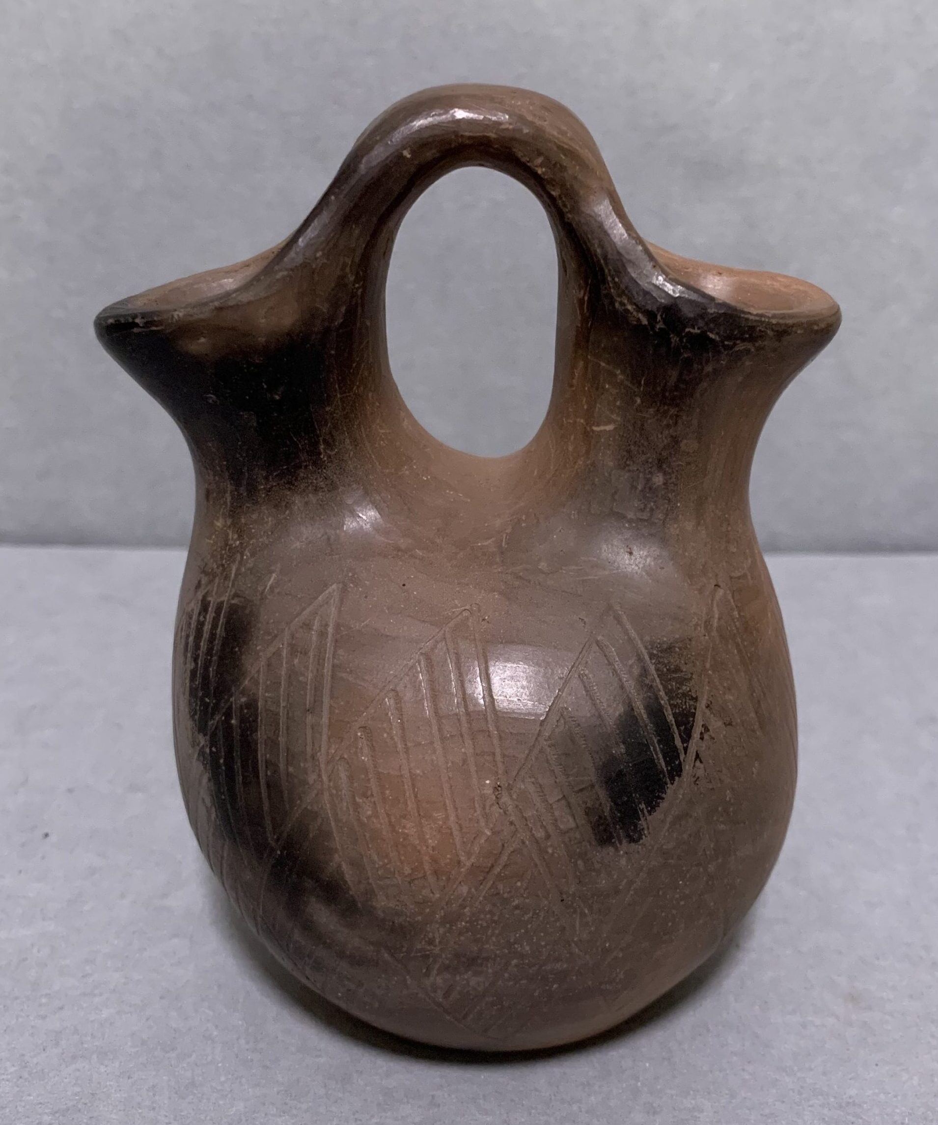unglazed brown ceramic vase with incised diagonal designs and two spouts connected by a handle