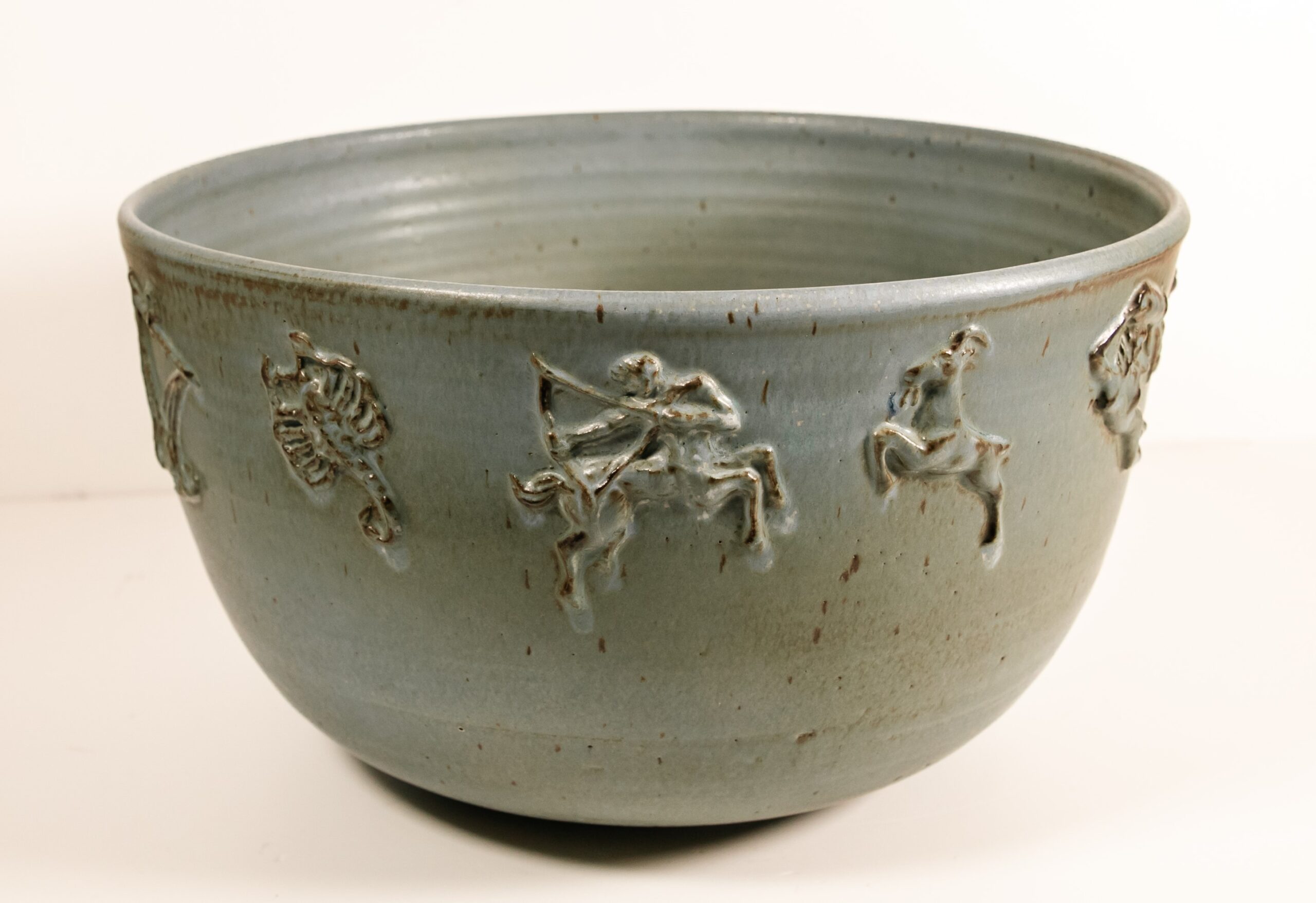 large mottled blue-gray ceramic punch bowl with raised zodiac designs on sides