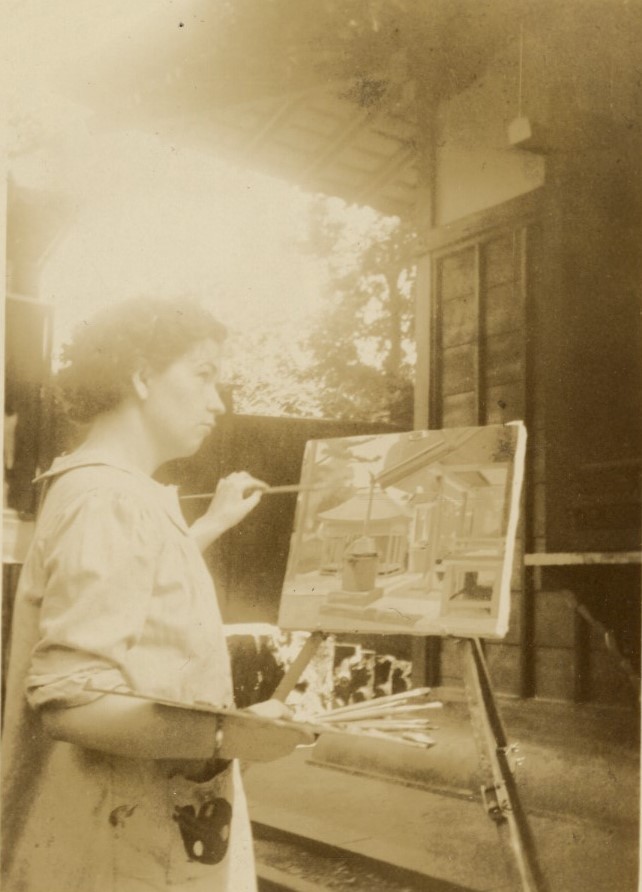 sepia-toned photograph of a woman in a painter's smock painting at an easel