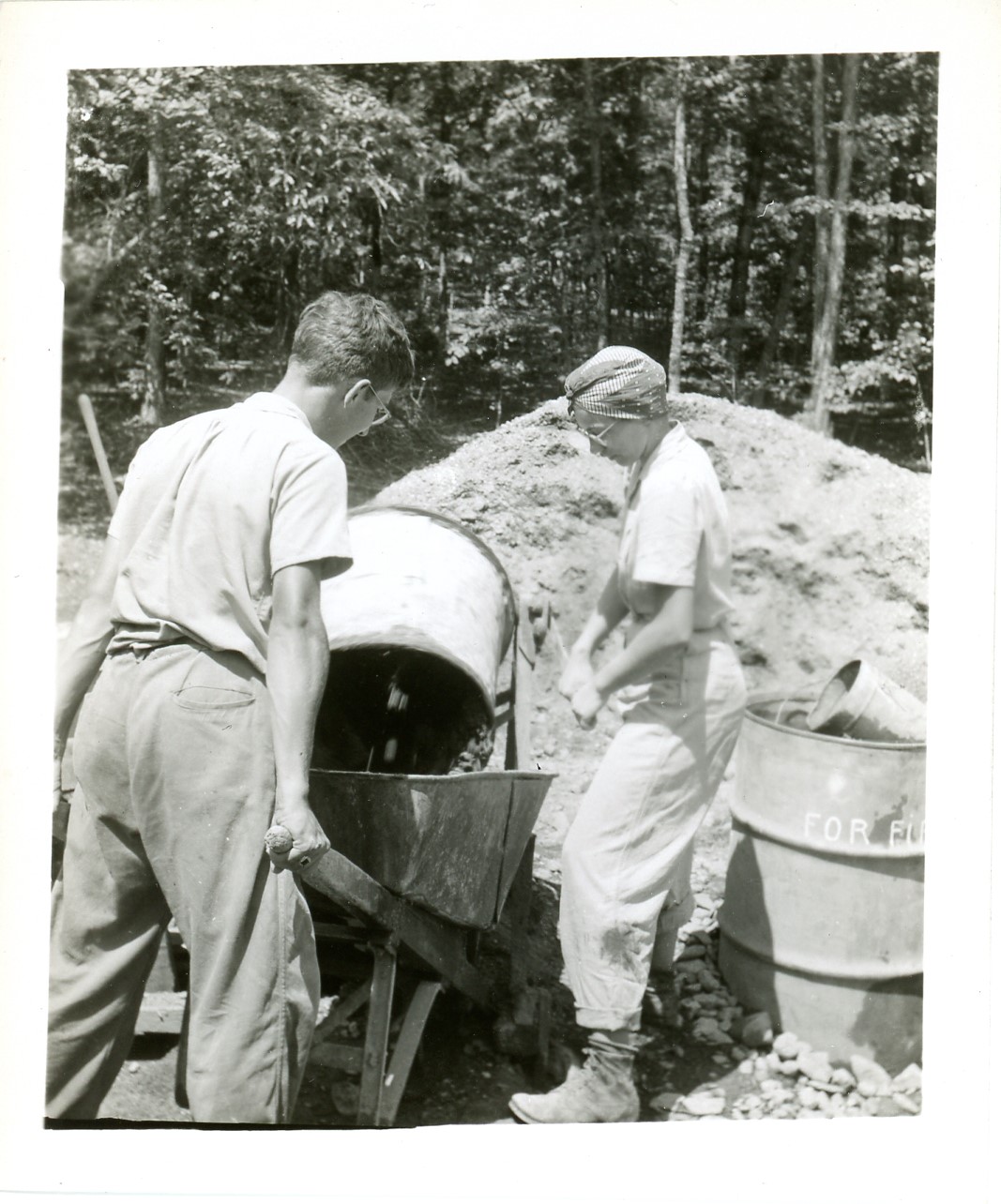 2025-45-005 black-and-white photo of a man and a woman in 1940s work clothes with a wheelbarrow and cement mixer