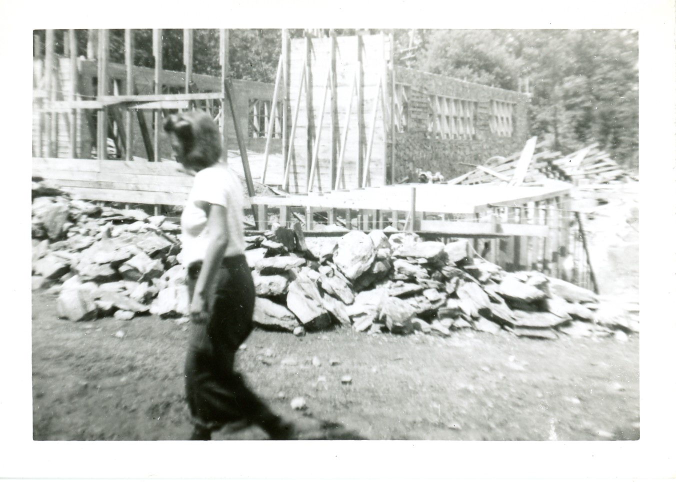 2025-45-021 black-and-white photo of a woman walking in front of a stone and frame construction site