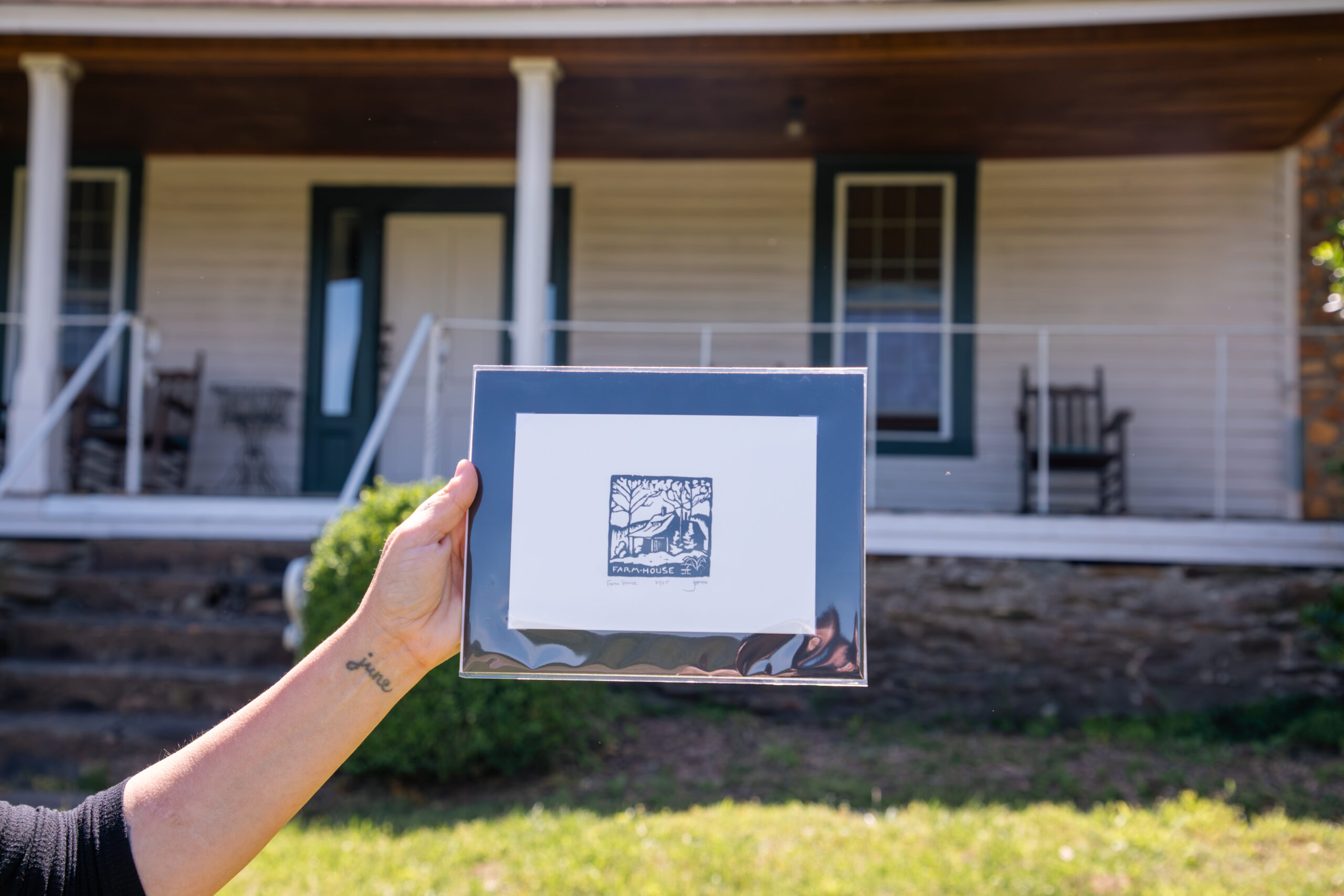 woodblock print held up in front of the white frame house with front porch that it depicts