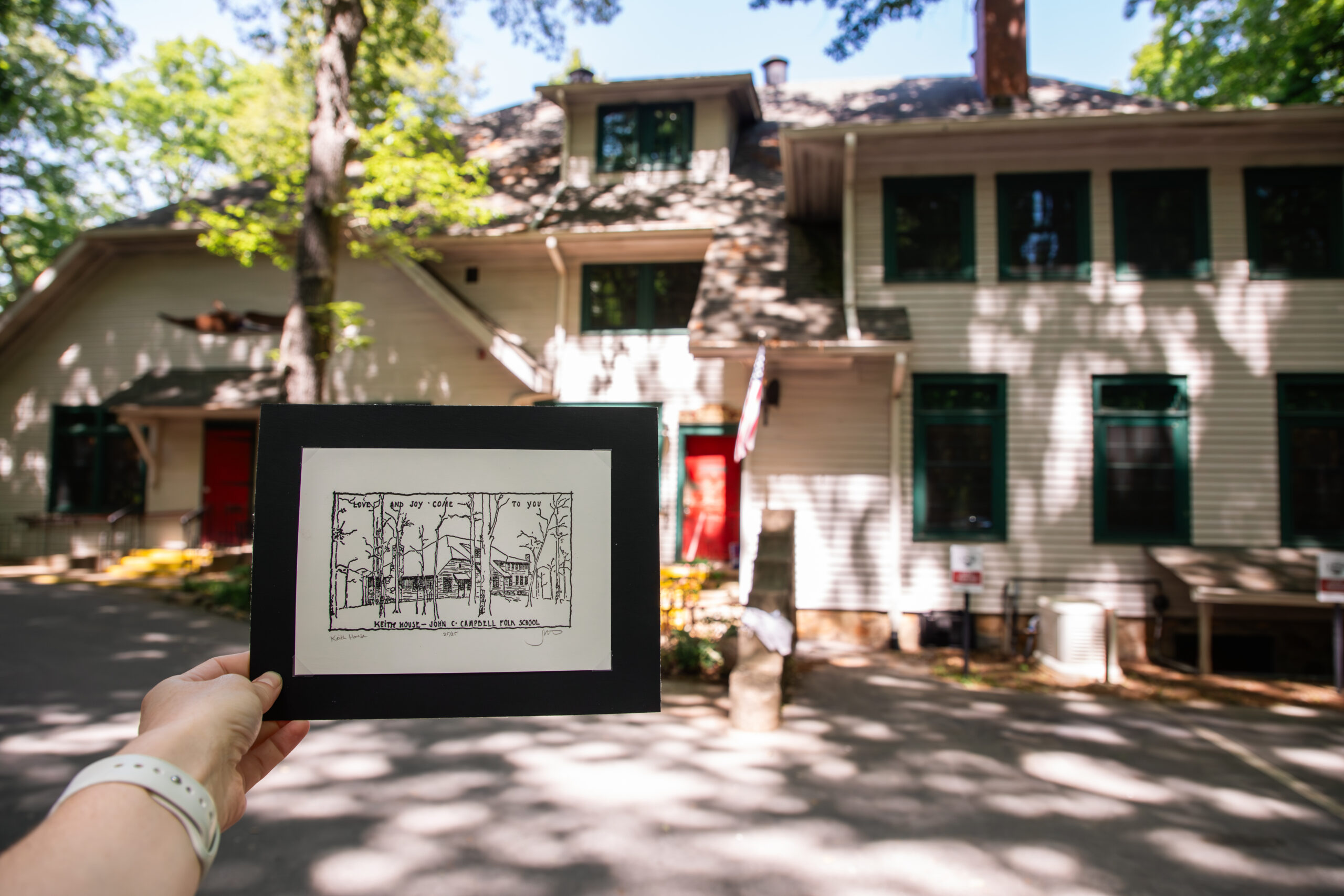 woodblock print held up in front of the two-story white frame building that it depicts