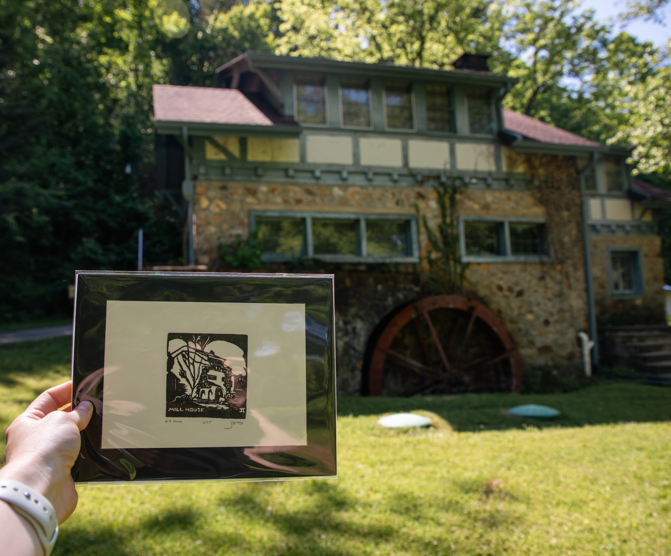 woodblock print held up in front of the two-story stone house with water wheel that it depicts