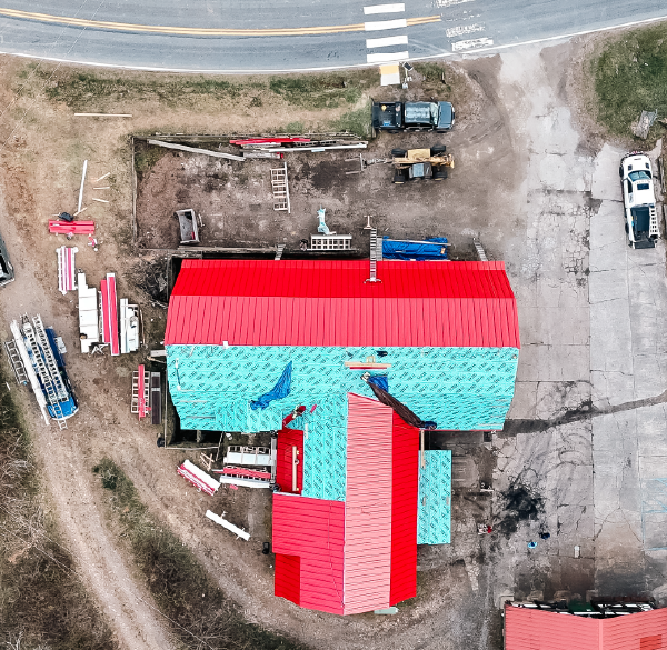 Aerial view of a construction site featuring a building with a red and blue roof near a road.