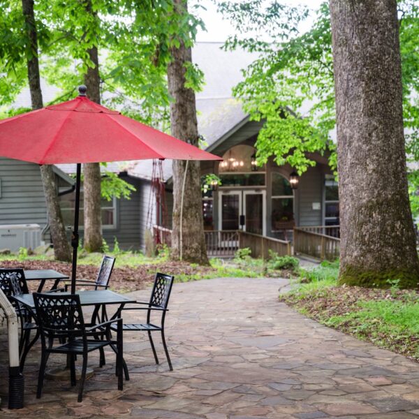 Path leads to a building with outdoor seating under a red umbrella, surrounded by trees. Possible folk school setting.